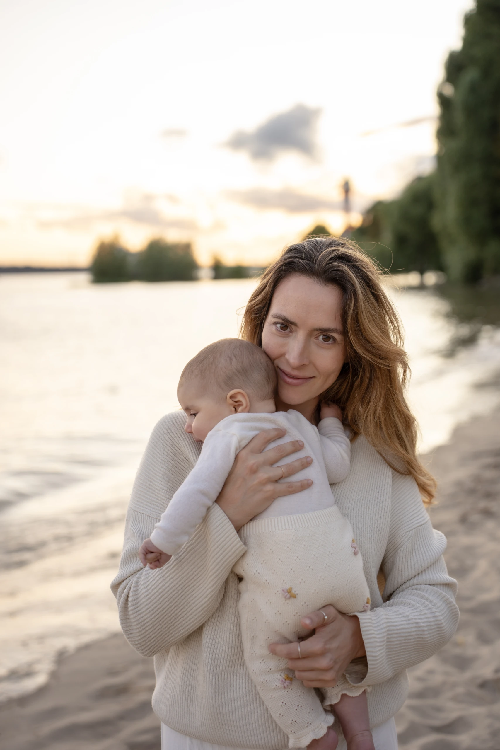 Mutter hält ihr Baby liebevoll im Arm bei einem Familienshooting am Wasser.