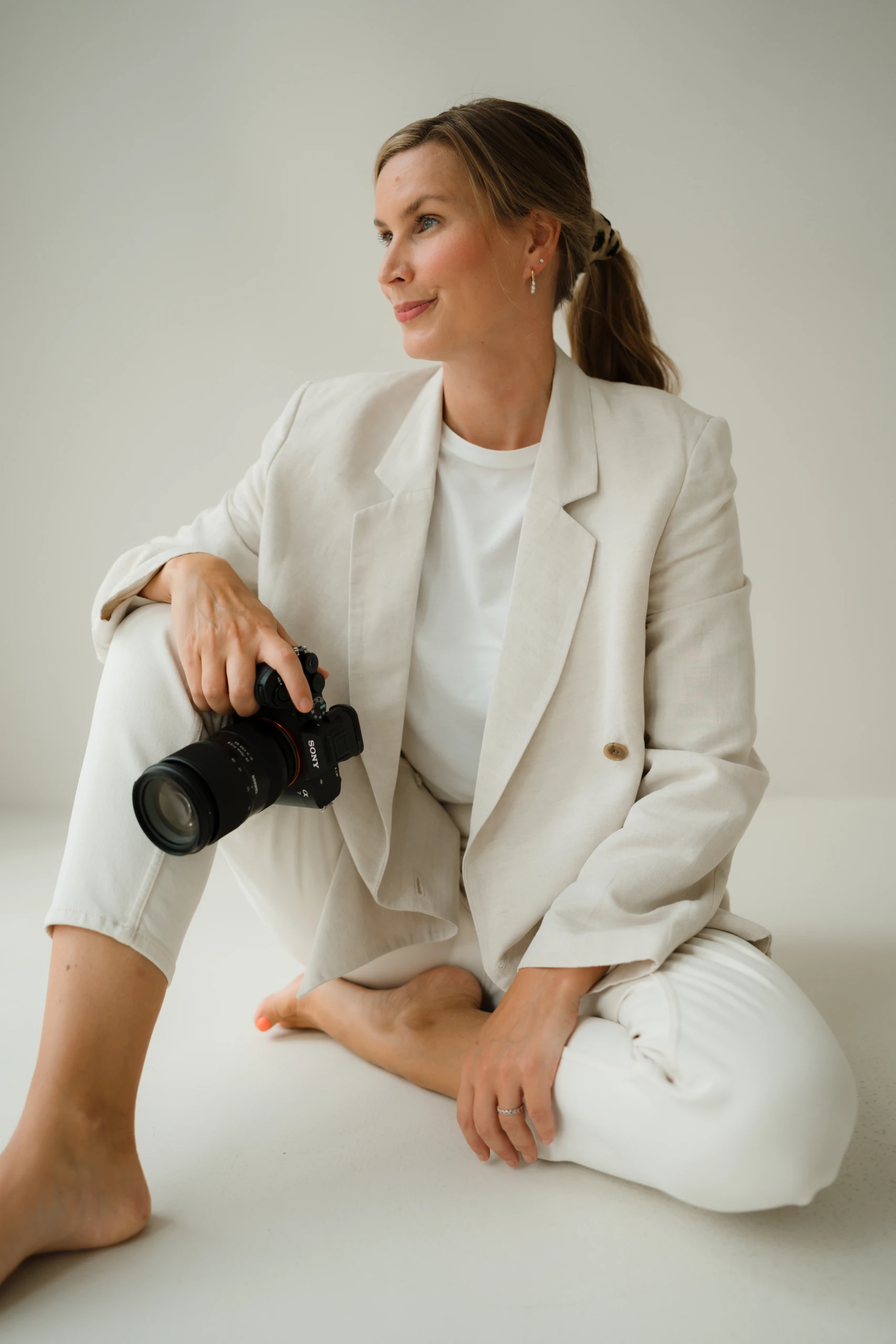 Fotoatelier Fuchs – Jana, Fotografin aus Hamburg Jana von Fotoatelier Fuchs sitzt in heller Kleidung mit ihrer Kamera in der Hand.