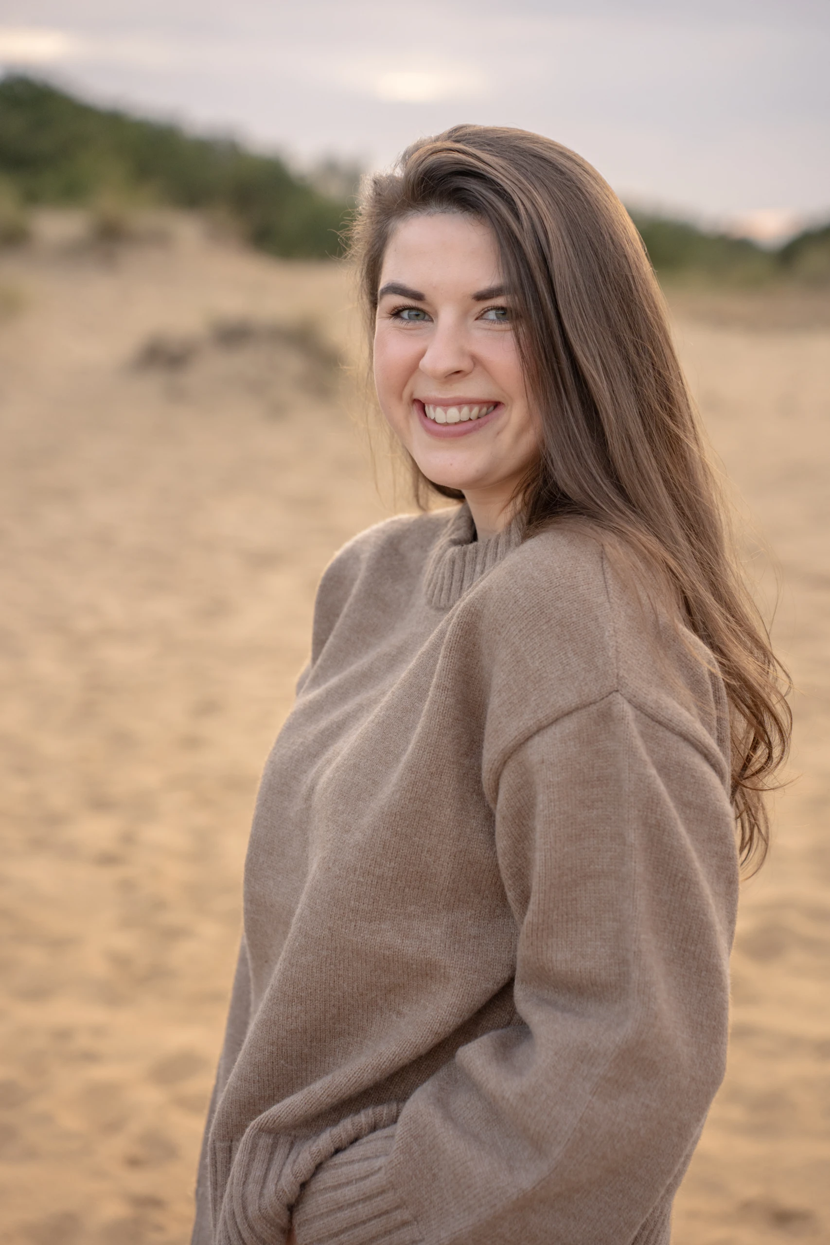 Natürliches Portrait einer lächelnden Frau in einer sandigen Outdoor-Kulisse.