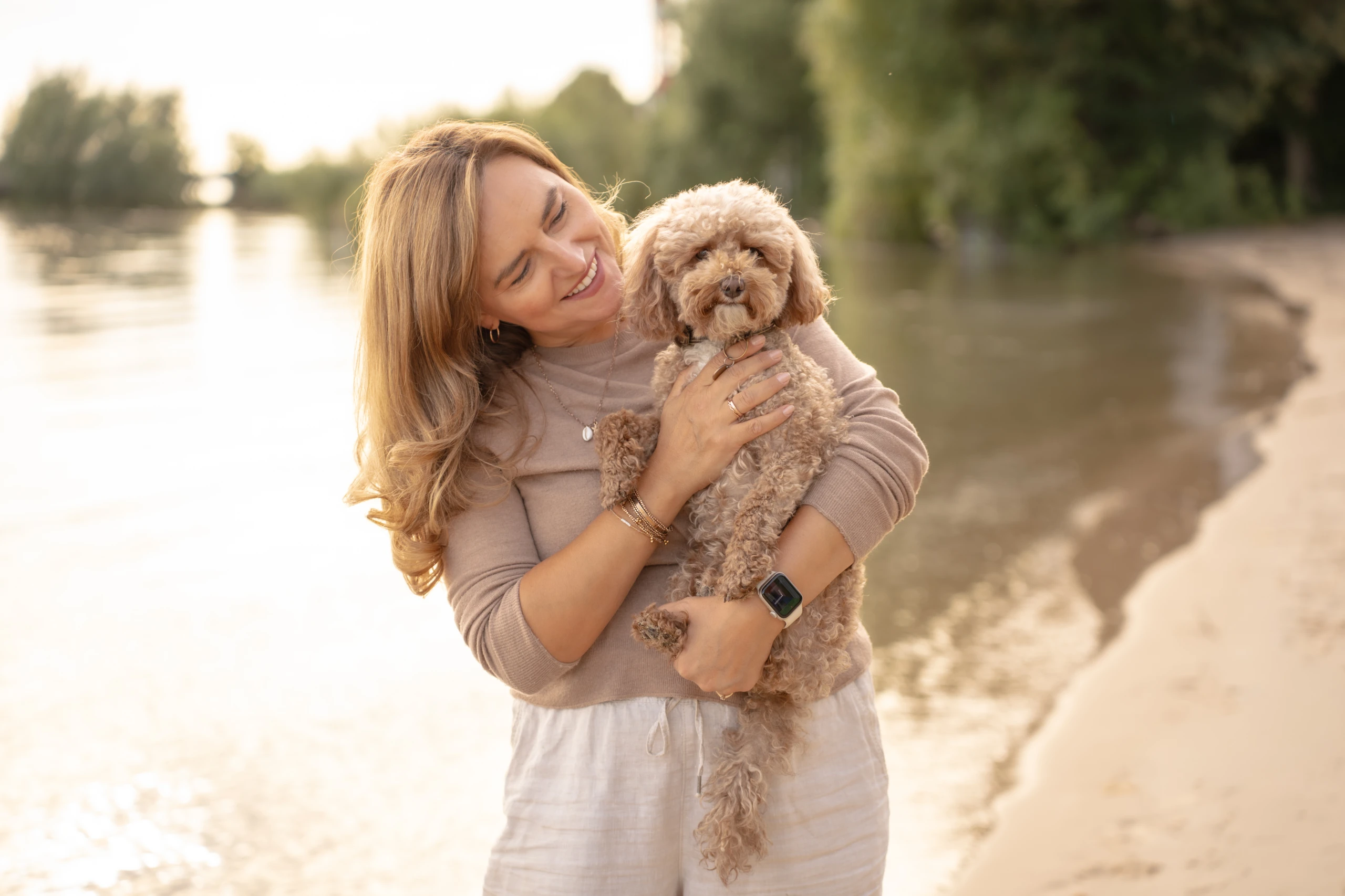 Frau hält ihren kleinen Hund im Arm bei einem natürlichen Tiershooting am Wasser.